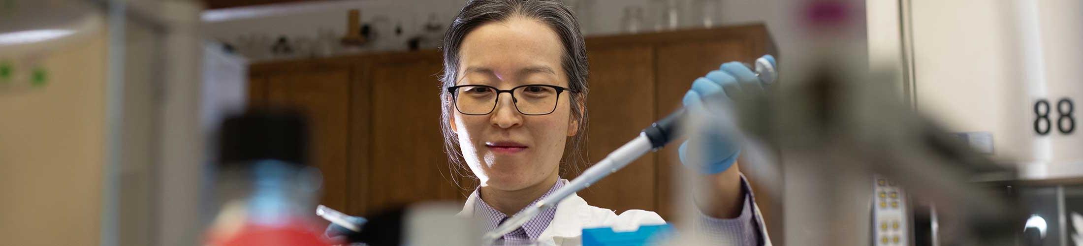 Researcher working in the lab holding a dropper with gloves on.